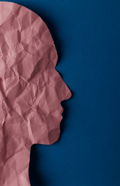 istock Crumpled pink paper shaped as a human head with copy space on blue paper background. 1298249107