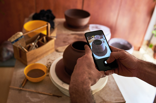 Shot of an unrecognisable man taking pictures of his finished products with a smartphone in a pottery studio