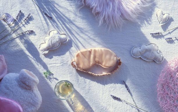 istock Healthy night sleep creative concept. Off white, ivory textile background. Pink silk sleep mask, tea, glass,. Soft toys, clouds and heart. Fluffy bottle warmer, fake fur. Dry lavender flowers and oil 1298251808