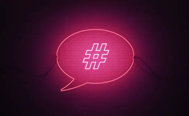 Speech bubble shaped pink neon light with hashtag symbol on black wall. Horizontal composition with copy space. Online messaging concept.