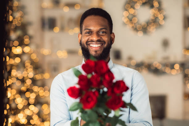 smiling black man holding roses, giving to camera - men african descent giving flower imagens e fotografias de stock