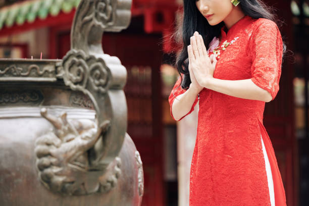Cropped image of young pensive woman in traditional red dress praying outdoors at temple