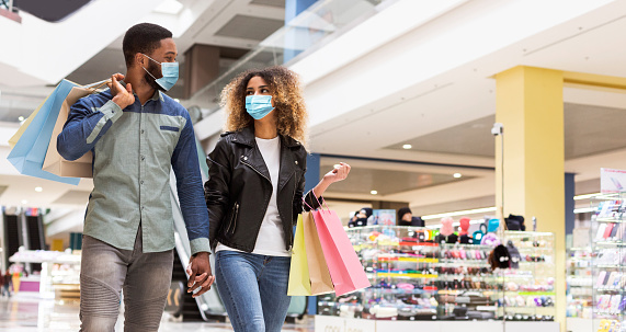 African american loving couple in protective face masks spending time together after shopping in mall center, panorama with free space. Black man and woman walking by shopping mall during quarantine