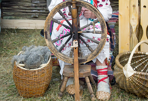 Near an old spinning wheel sits an elderly woman in national costume and worked on it, spinning.