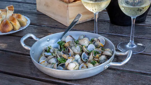 Photo of Recipe for cockles with garlic and parsley in an aluminium casserole dish, accompanied by a champagne drink