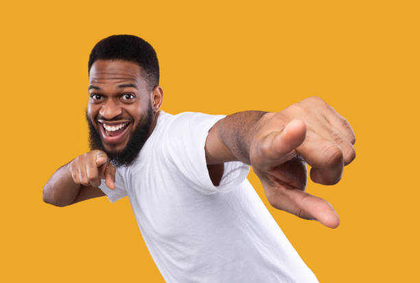 lustige afrikanische mann posiert zeigefinger auf kamera, gelben hintergrund - zeigen stock-fotos und bilder
