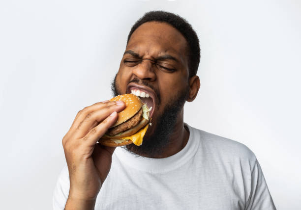 istock African Man Biting Burger Enjoying Junk Food Over White Background 1298255687