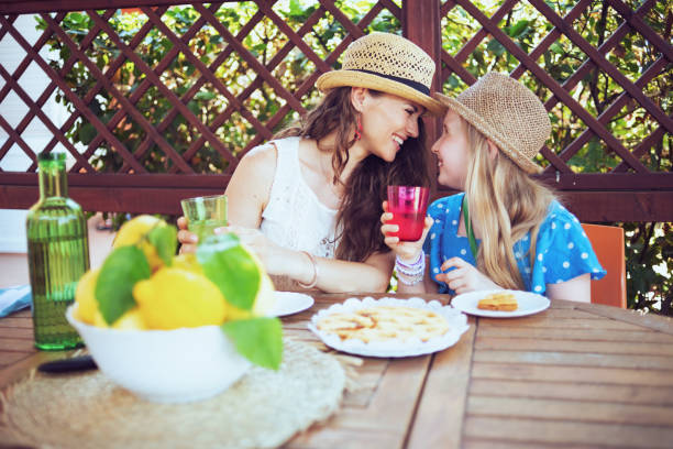 happy trendy mother and daughter sitting at table having lunch happy trendy mother and daughter with crostata, green bottle of water and plate of local farm lemons sitting at the table having lunch in the patio. crostata photos stock pictures, royalty-free photos & images