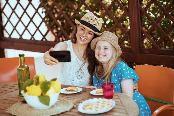 smiling family having online meeting and having breakfast smiling modern family with crostata and plate of local farm lemons having online meeting on a smartphone and having breakfast in the terrace of guest house hotel. crostata stock pictures, royalty-free photos & images