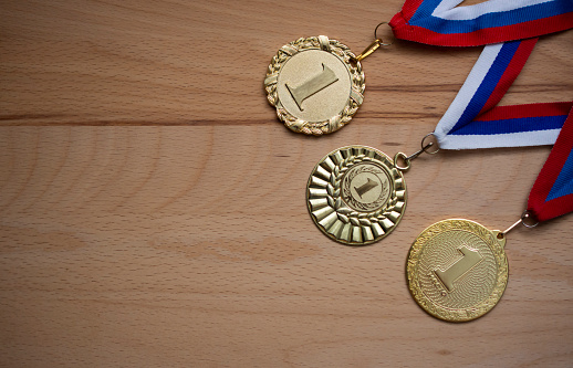 golden medals for first place with three colored ribbon white, red and blue on wooden background with free copy space
