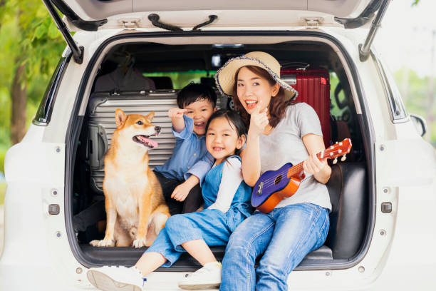 famiglia felice con cane shiba inu vicino all'auto all'aperto. una famiglia con madre, figlia e figlio che suonano musica sul retro dell'auto con shiba inu. - car family picnic vacations foto e immagini stock