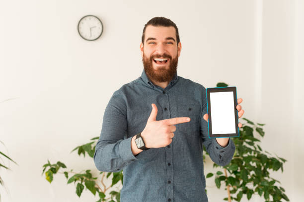 istock Happy office worker man pointing at white screen on tablet while standing in office 1298258266