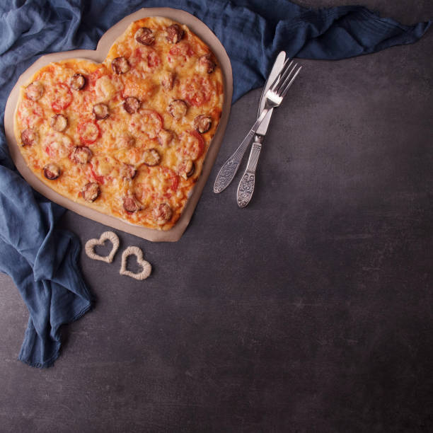 Romantic dinner in rustic style. Heart shaped pizza, blue napkin and cutlery on dark table