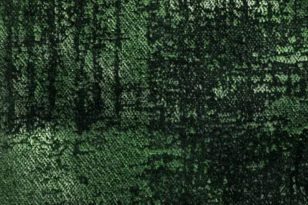 Dark green and olive fluffy background of soft, fleecy fabric. Texture of emerald velveteen textile backdrop with shiny pattern, closeup.