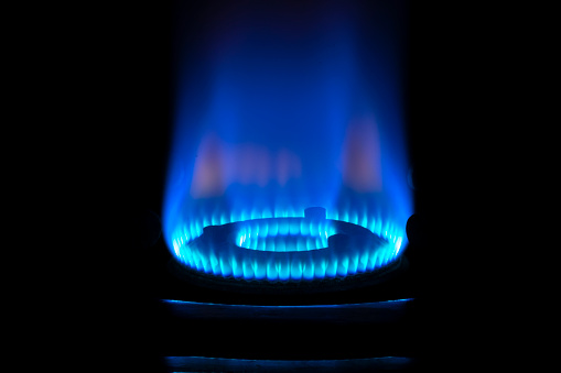 Close up of gas burner with blue flame on kitchen stove in dark.