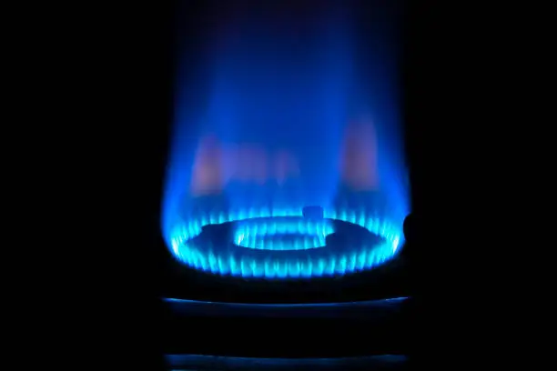 Photo of Close up of gas burner with blue flame on kitchen stove in dark.