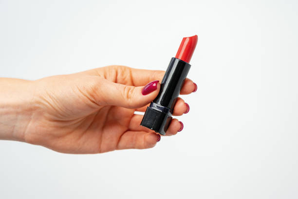 istock Female hand holding red lipstick against gray background 1298261782