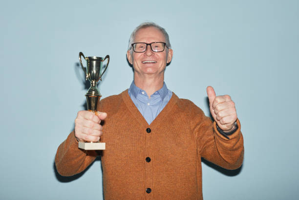 istock Cheerful Senior Man Holding Trophy Flash Shot 1298262472