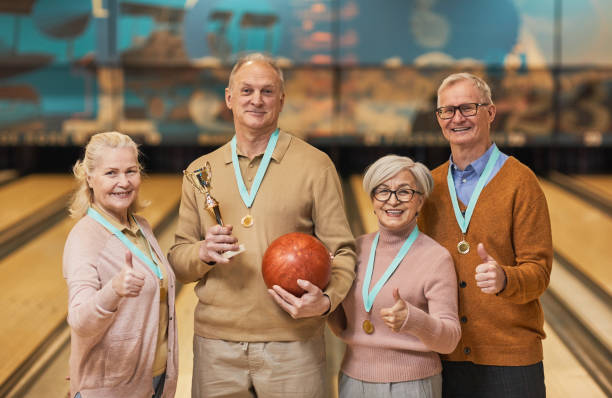 Senior Bowling Team Waist up portrait of smiling senior team wearing medals holding trophy and looking at camera while standing in bowling alley after winning match sports team event stock pictures, royalty-free photos & images
