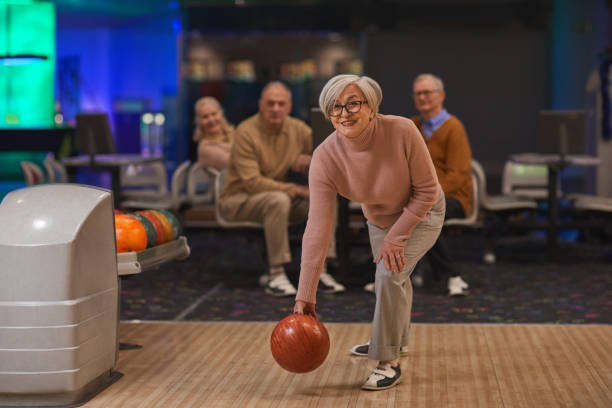 mujer senior jugando a los bolos con amigos - bowling holding bowling ball hobbies fotografías e imágenes de stock