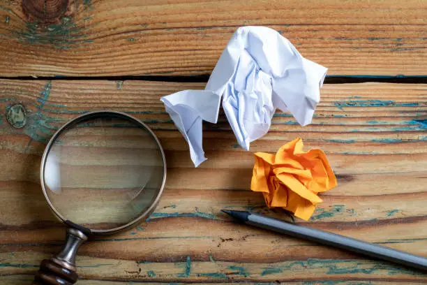 Photo of Crumpled paper, pencil and magnifying glass on a wooden background. Education, information and data search concep