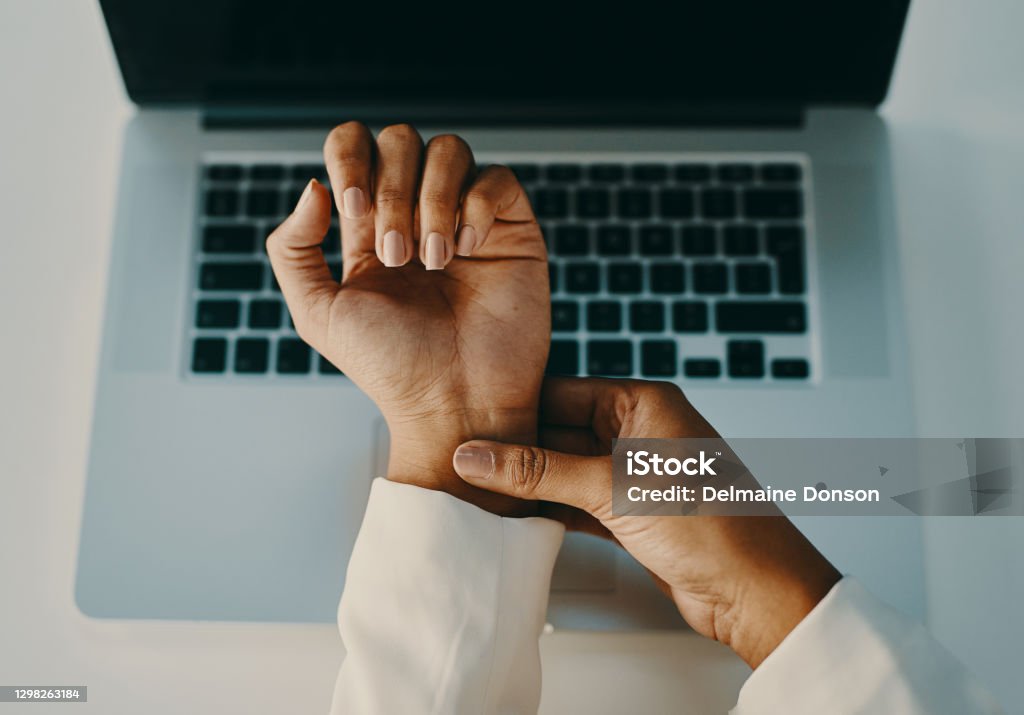 A little pressure could relieve the pain Shot of an unrecognisable businesswoman experiencing wrist pain while working in a modern office Hand Stock Photo
