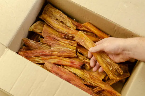 Photo of A man's hand pulls Dried Beef Tendon out of a cardboard box.
