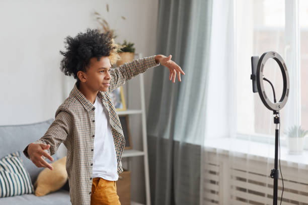 African-American Boy Filming Videoblog Side view portrait of teenage African-American boy filming videos at home and dancing to camera set on ring light, young blogger concept, copy space singing photos stock pictures, royalty-free photos & images