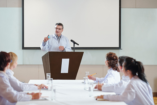 Senior researcher speaking at conference for medical workers and showing a vial of new vaccine his team was working on