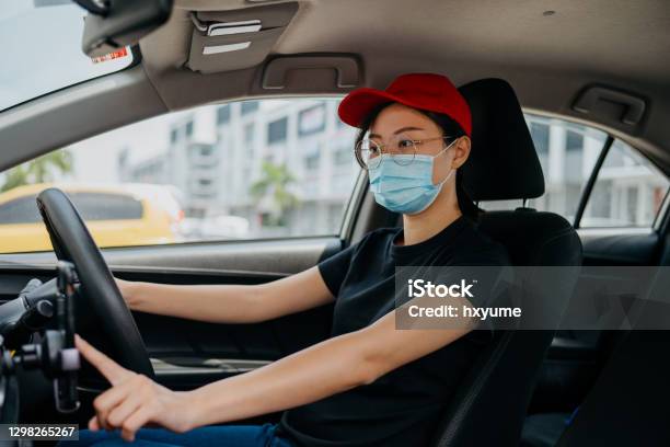 Female Driver Wearing Protective Face Mask And Using Smartphone For Taking Orders Stock Photo - Download Image Now