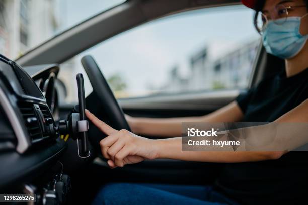 Female Driver Wearing Protective Face Mask And Using Smartphone For Taking Orders Stock Photo - Download Image Now