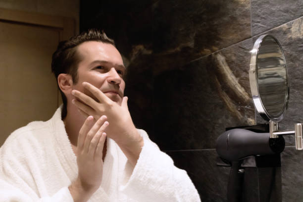 istock Reflection in a mirror of a man applying moisturizer on his face in the bathroom. 1298266396