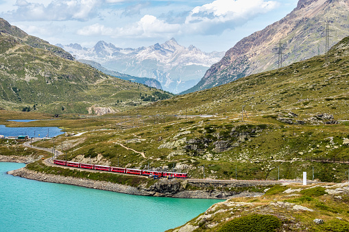 Bernina , Switzerland - Aug 01, 2020: Bernina Express train at the White Lake in Ospizio Bernina, upper Engadin, Graubuenden, Grisons, Switzerland.