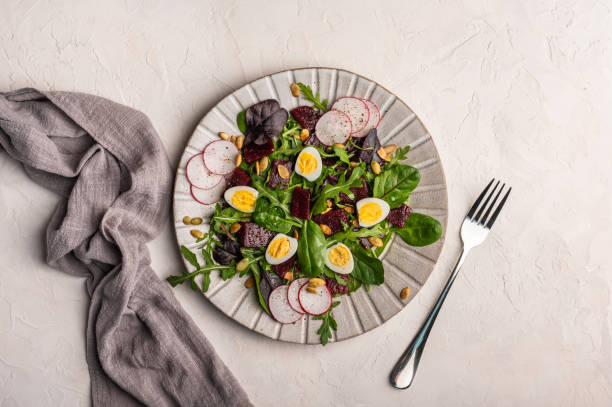 Homemade salad of quail eggs, boiled beetroot, arugula and basil Homemade salad of quail eggs, boiled beetroot, radish, arugula and basil with olive oil served with linen napkin and fork on a light background, top view, copy space quail egg stock pictures, royalty-free photos & images