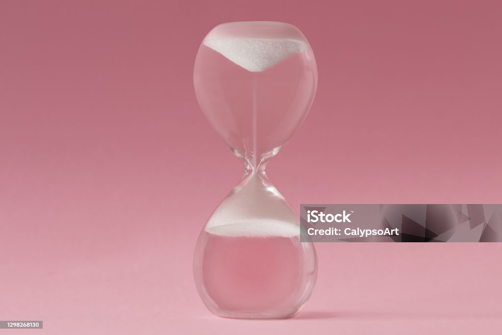 Upside-down hourglass on pink background - Concept of reverse time Aging Process Stock Photo