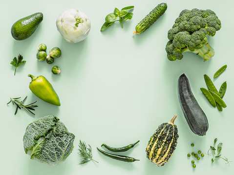 Green monochrome flat lay composition with vegetables, copy space in center. Vegetables - green peas, zucchini, avocado, bean-pod, pumpkin, broccoli, brussels sprouts, rosemary, microgreens. Top view