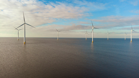 Aerial view on offshore wind turbines off the coast of Flevoland on the IJsselmeer coast in The Netherlands during a beautiful day with clouds in the sky.