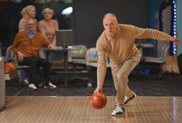 sportive senior man jugando a los bolos con amigos - bowling holding bowling ball hobbies fotografías e imágenes de stock