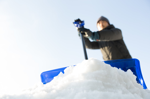 man removing snow with a blue shovel