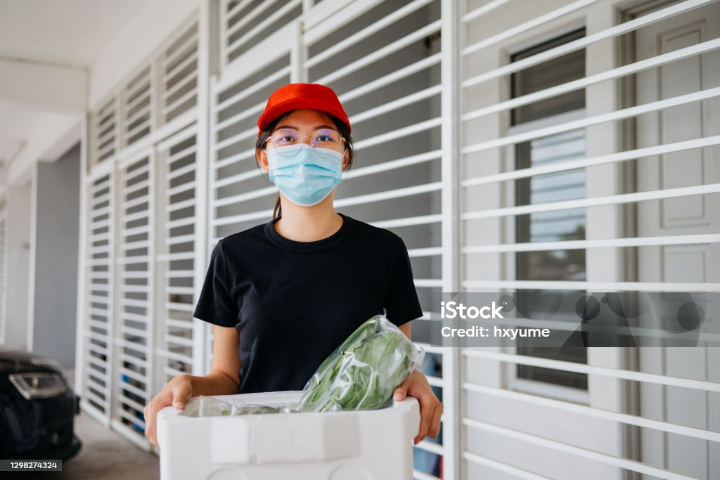 An Asian Chinese delivery person holding a box of fresh vegetables Image of an Asian female delivery person holding a box of fresh vegetables ready for delivery 30-34 Years Stock Photo
