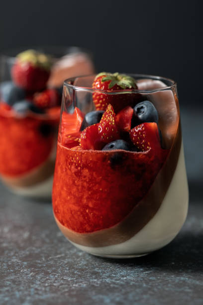Double-layer vanilla and chocolate panna cotta dessert with with strawberry puree, fresh blueberries and strawberries stock photo