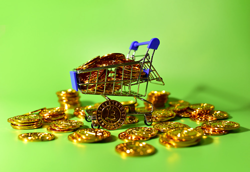 Shopping cart with bitcoin gold crypto coins. BTC cryptocurrency investing concept in mini shopping trolley. Blockchain and financial technology. Make a lot of money, be rich and spend dollars