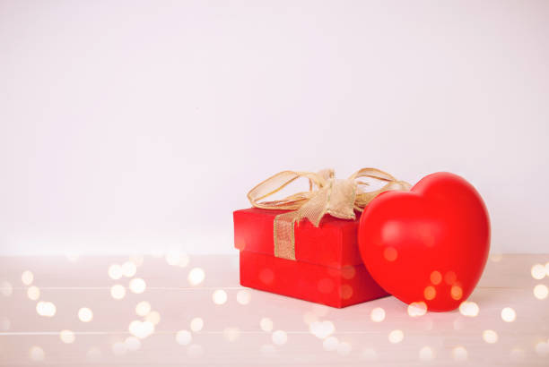 Red gift box and heart shape on wooden table with bokeh background, love and romance, presents in celebration and anniversary with surprise on desk, happy birthday, valentine day concept. san valentín, regalos, amor, regalo, caja, donar, caridad, ayuda, donante, cumpleaños, cinta, felicitar, sorpresa, paquete, copyspace, vacaciones, rojo, madera, fondo, corazón, forma, madera, copiar espacio, espacio, saludo, decoración, arco, celebraci