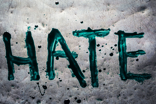 The word hate painted by green paint on old metal table