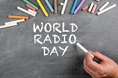 World Radio Day, 13 February. White chalk in a man's hand and a chalk board in the background