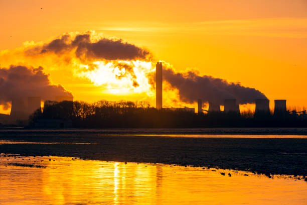 amanecer en invierno sobre drax en el norte de yorkshire con el sol saliendo detrás de un rastro de vapor de agua de las torres de refrigeración de una planta de energía.  reflejos dorados en aguas estancadas en campos agrícolas. - sky landscape horizon over water sunlight fotografías e imágenes de stock