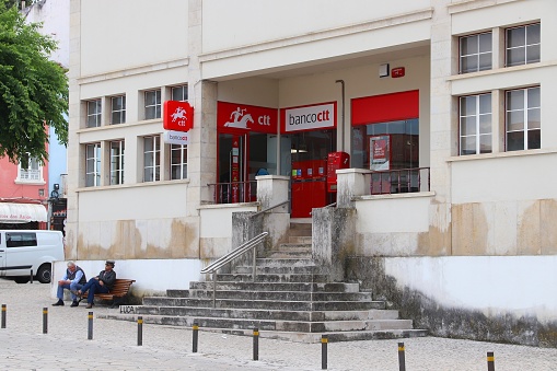 People sit in front of CTT Correios de Portugal (national postal service) and Banco CTT (banking and financial services) branch in Nazare.