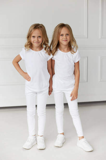 istock Two twin sisters in white clothes holding hands isolated on a white background. Vertical view. 1298288887