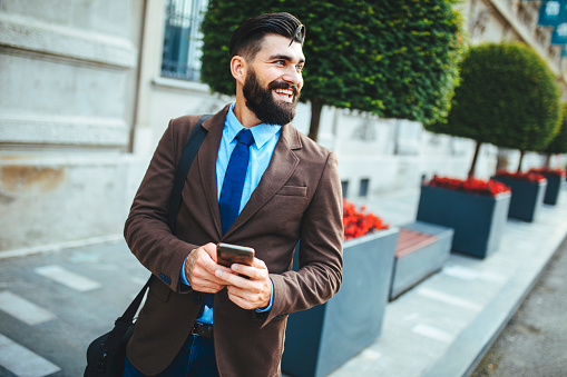 Smiling businessman texting outdoors in the city