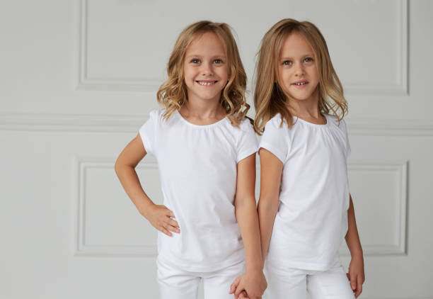 istock Two twin sisters in white clothes holding hands isolated on a white background. Horizontal view. 1298289410